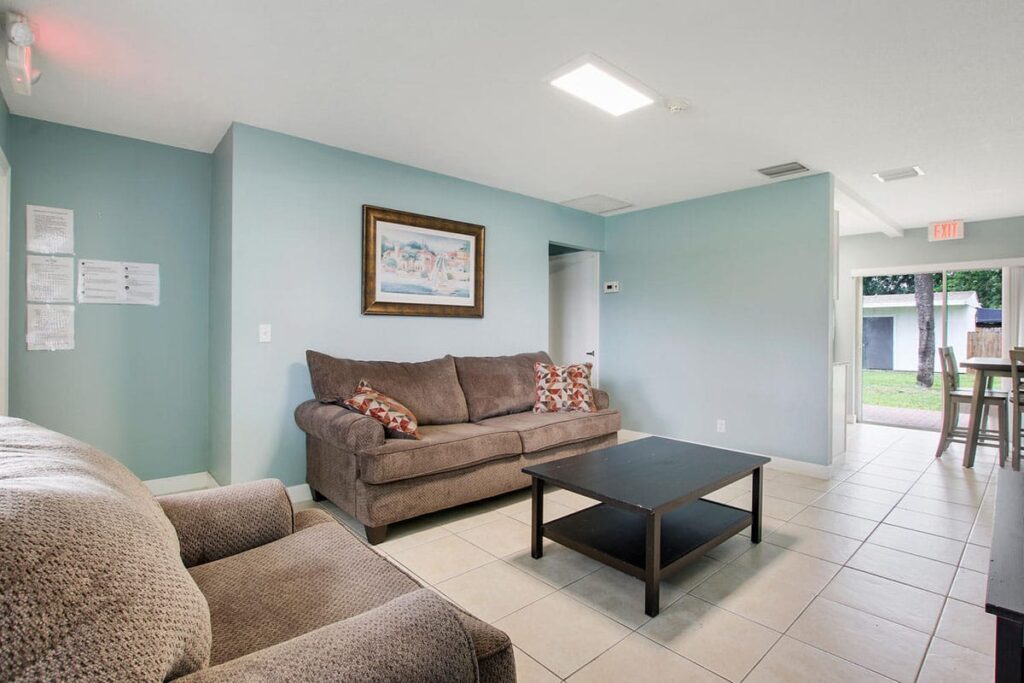 a pair of couches in a common area with a table, painting, and sliding door