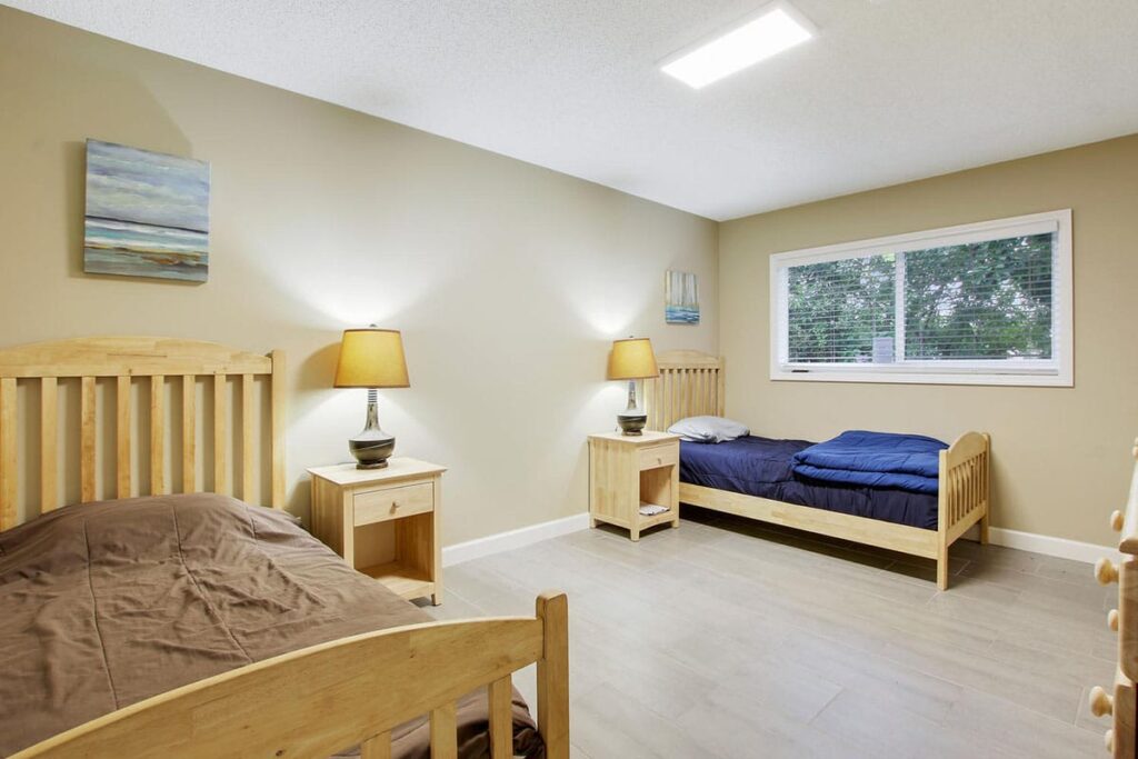 two beds in a bedroom with lamps, nightstands, and a large window