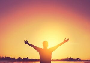 a person in an alumni program stands with outstretched arms at sunrise